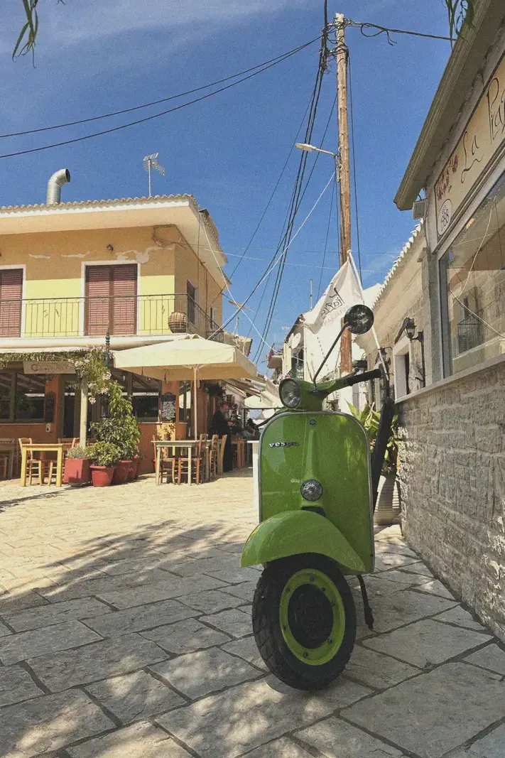 A quaint alley in Lakka with a green scooter parked outside charming local shops, epitomizing the leisurely pace and inviting atmosphere of the village