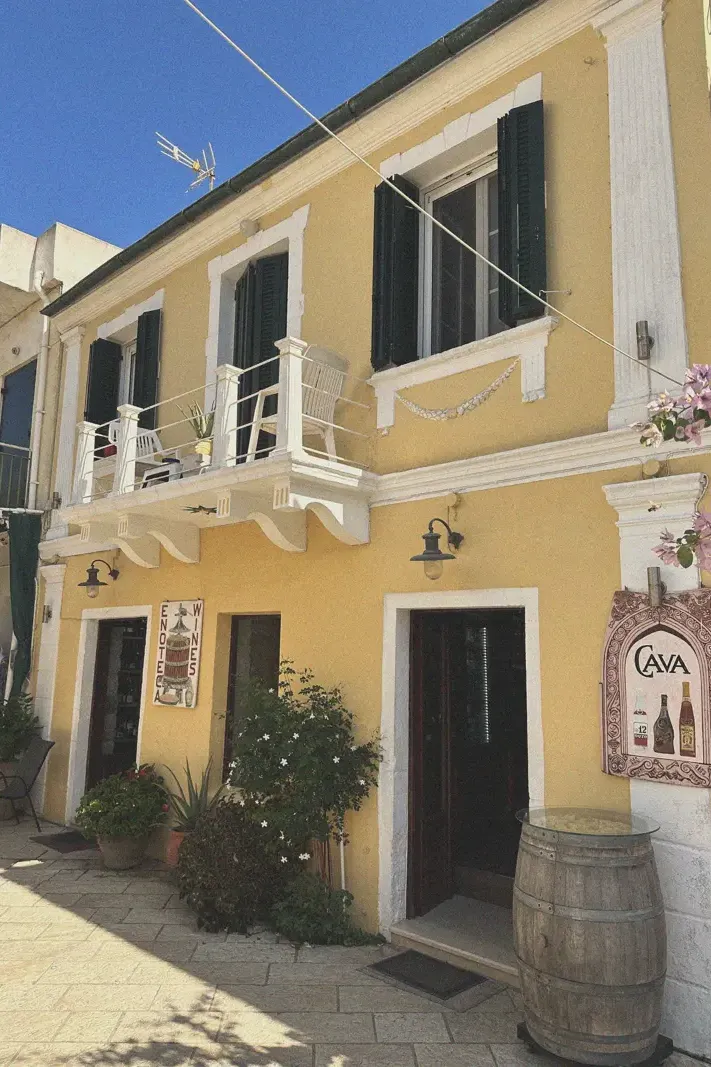 A two-story yellow building with a wine shop on the ground floor in Lakka, displaying the local architecture and village commerce