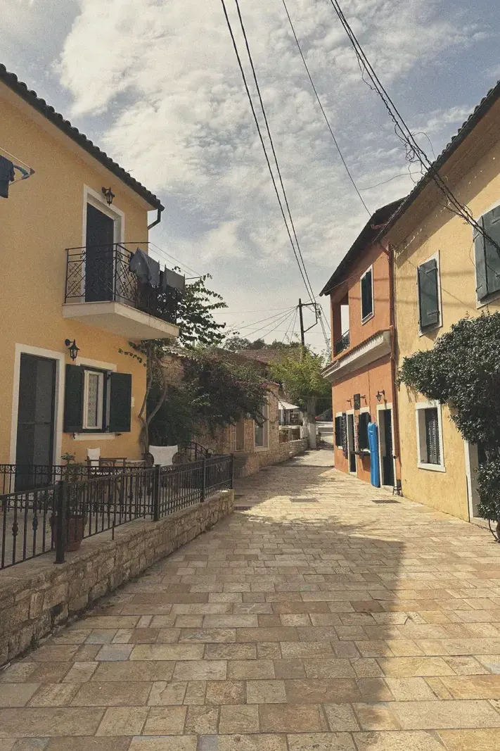 Narrow street in Loggos flanked by yellow and orange houses with shuttered windows and potted plants