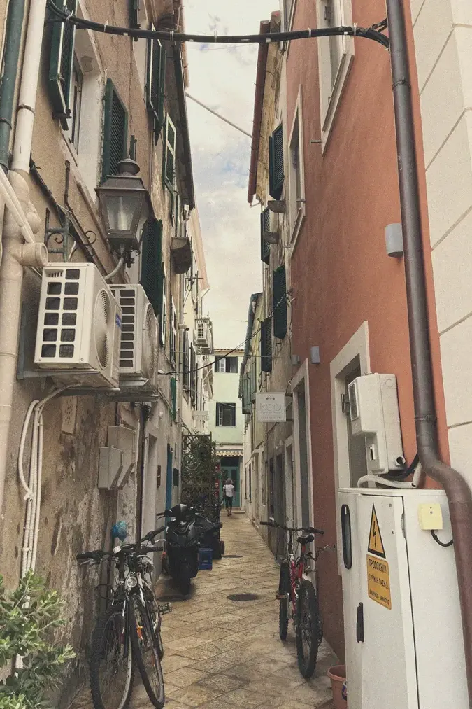 A narrow, stone-paved alley in Paxos, lined with bicycles and local residences, evoking the quaint village atmosphere.